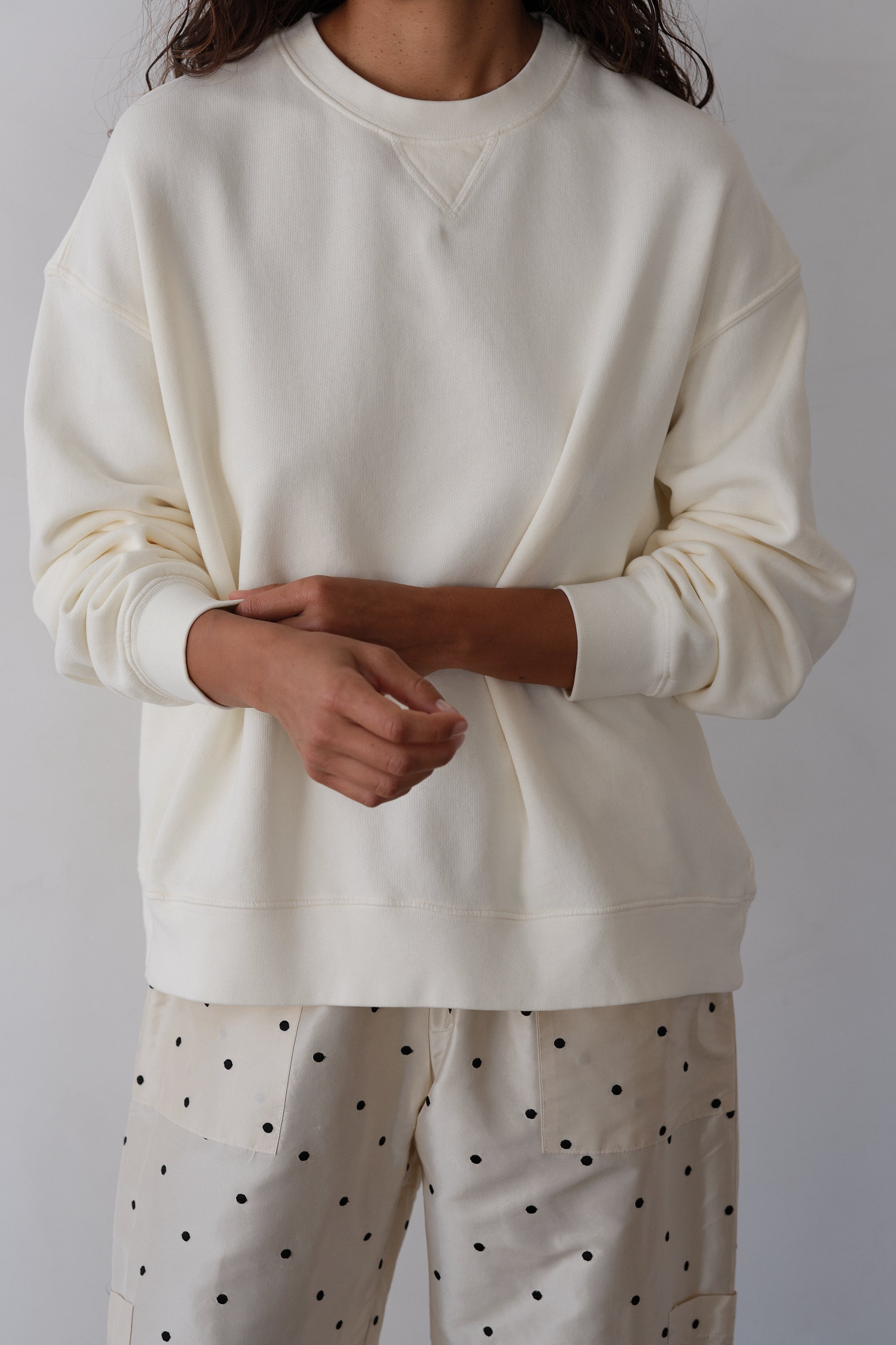 Person wearing a white sweatshirt and polka dot pants against a plain background